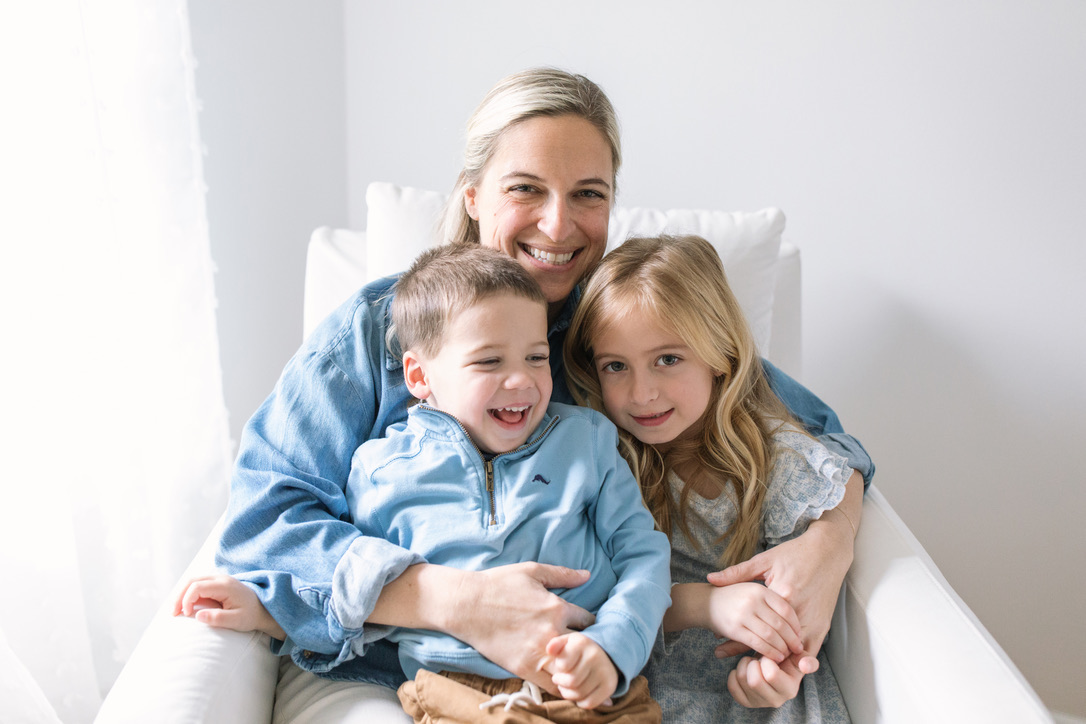 Emily Boesner, RN, smiling in a white armchair with her son and daughter.